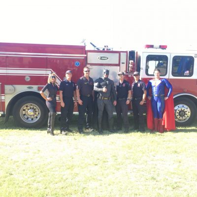 Lubbock batman, Superman, and catwoman in front of a Lubbock firetruck with first responders